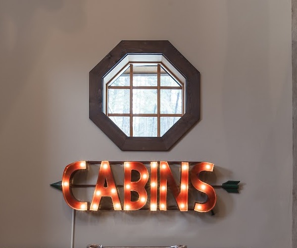 Illuminated marquee CABINS sign beneath a mirror in a styled entryway